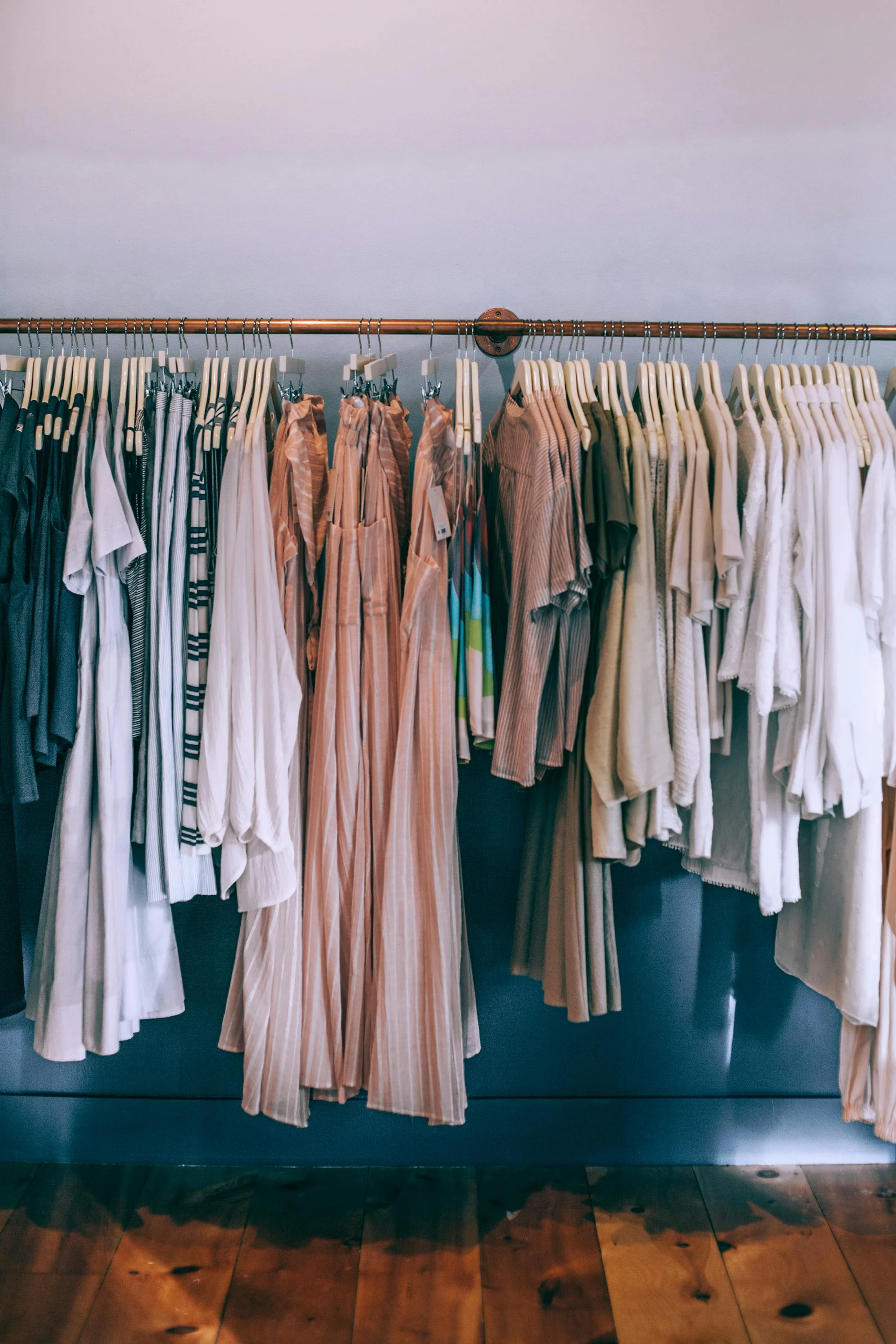 Neutral toned clothing displayed on wooden hangers in a boutique setting